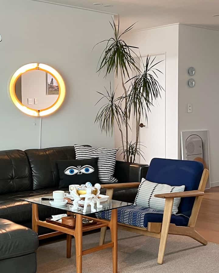 Modern living room with black leather sofa and wood tone furniture, featuring a blue fabric armchair and green plant adding natural vibe