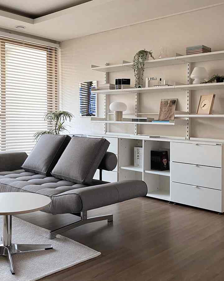 White and gray toned living room home office featuring modern sofa and shelving with clean, organized interior
