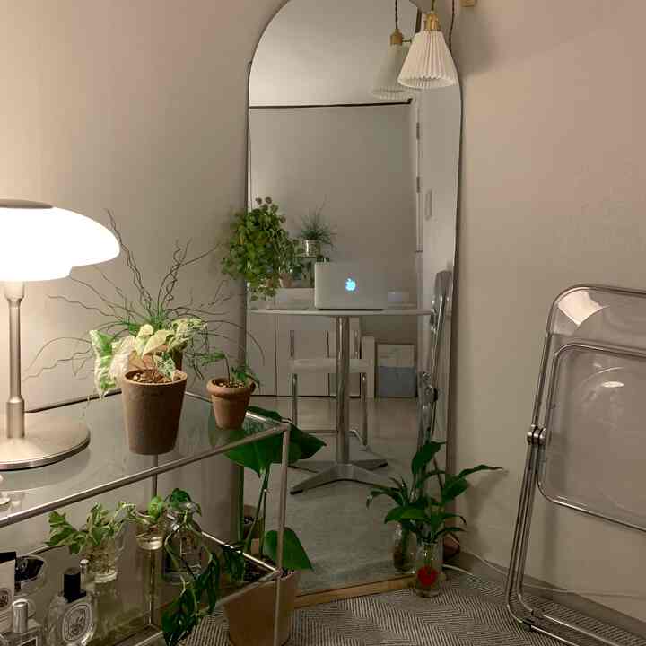 ナチュラルな色調のワンルーム、植物と円形テーブル、透明な椅子が配置された落ち着いたミニマルな空間