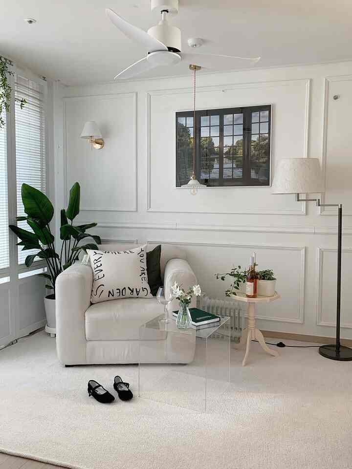 明るく白を基調としたリビング、ふわふわな白いラグと一人掛けソファ、透明なコーヒーテーブルと植物が配置されたシンプルな空間