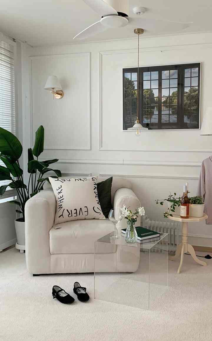 白と緑の色調のリビング、一人掛けソファと透明なアクリルテーブルが中央に配置され、壁にはポスターとブラケットライトがある印象的な空間