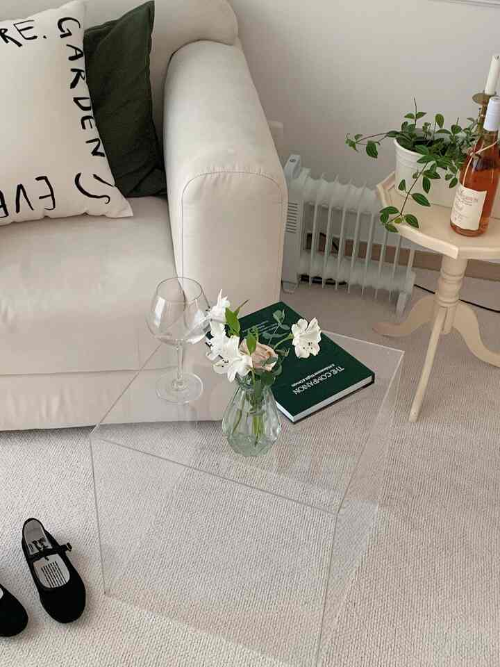 White and beige natural modern living room featuring a transparent acrylic table, white sofa, and wooden side table in a clean layout