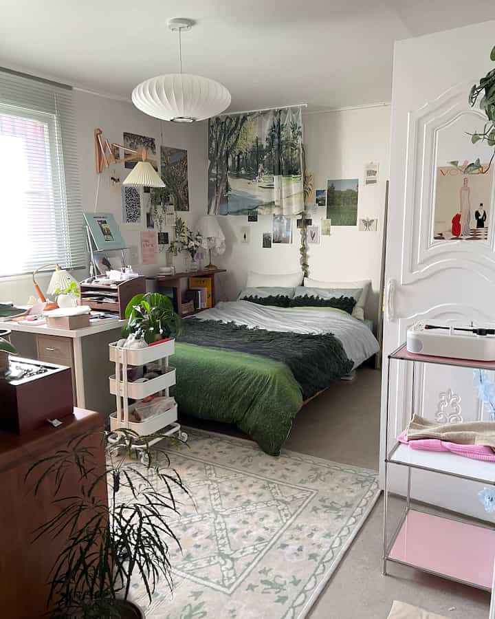 White and green toned studio bedroom featuring bed, desk, rug, and plants arranged naturally in a compact space