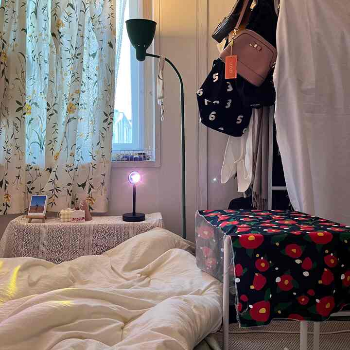 A white and beige toned bedroom featuring a bed, floor lamp, and floral curtains creating a cozy atmosphere