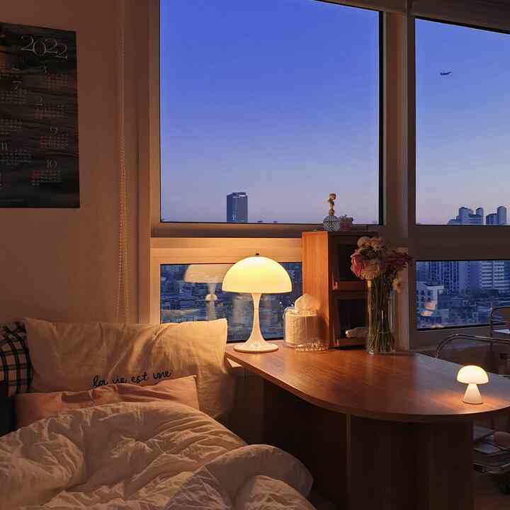 Cozy studio bedroom with warm lighting, wood furniture, and large windows offering a city view