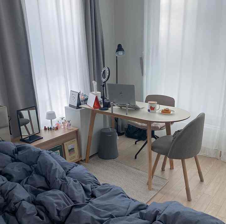 ホワイトとグレーの色調のワンルーム寝室、木製デスクと椅子が配置された自然なモダンなホームオフィス空間