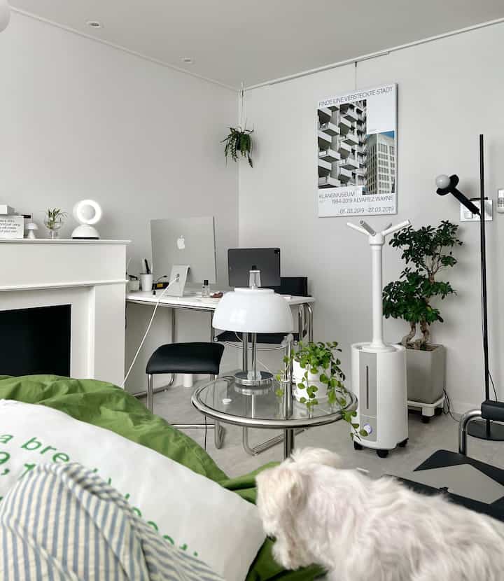 Minimalist white-toned home office and living room featuring a glass coffee table lamp and plants, creating a clean interior