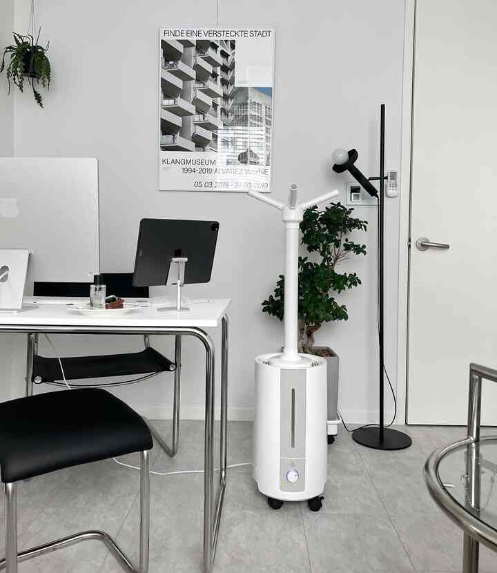 White-toned home office space featuring a desk, black chairs, a humidifier, and a floor lamp in a clean interior
