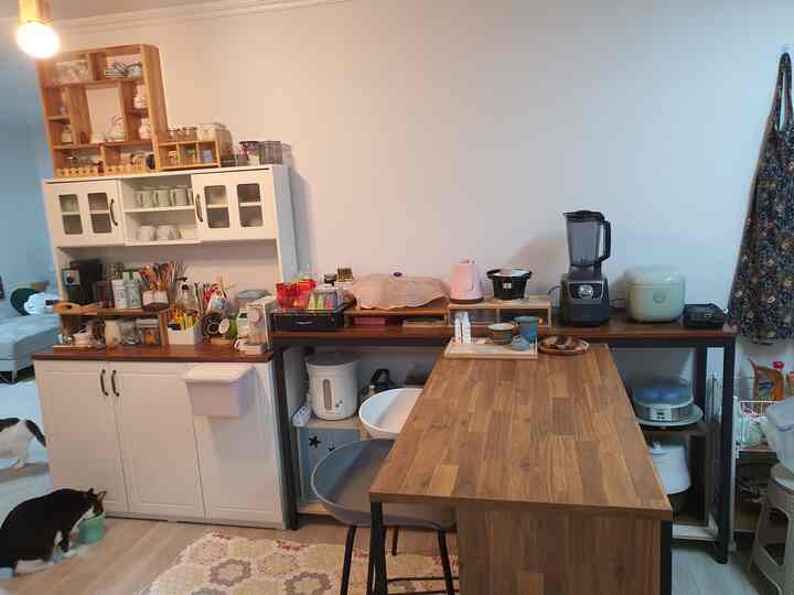 白い壁と木目調の調理台が調和するキッチン、バースツールや多様な調理器具が配置された雰囲気のある空間