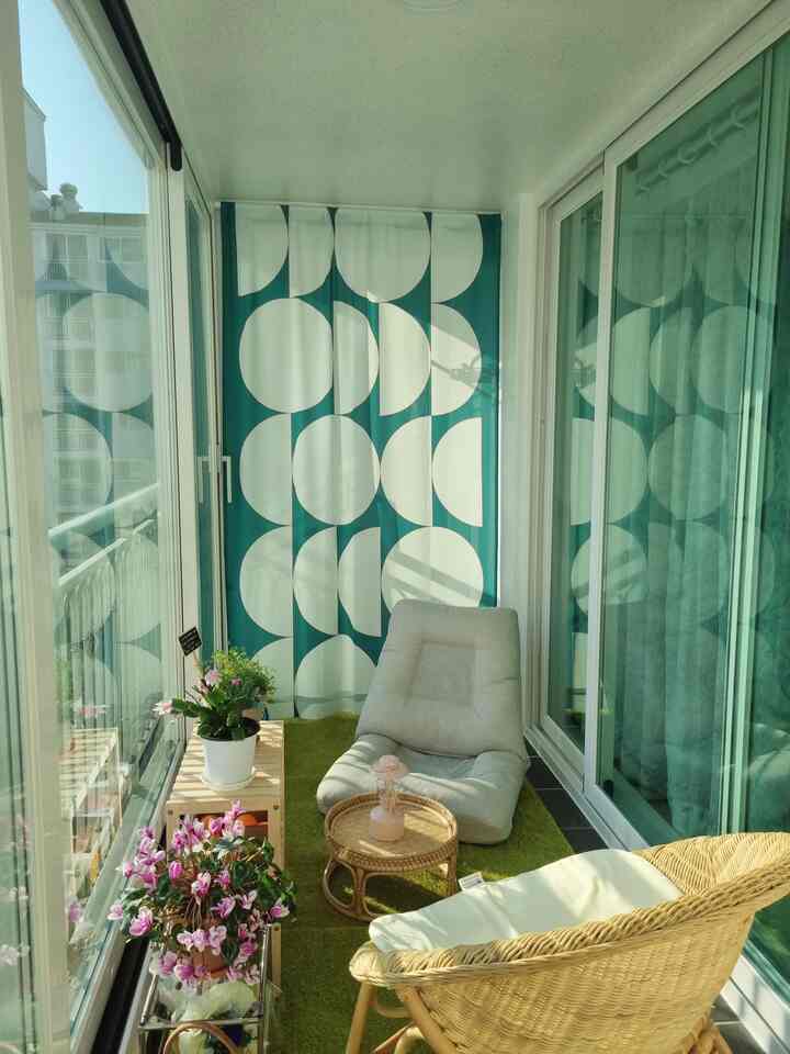Cozy veranda featuring green grass rug, wooden shelves, and rattan table with natural sunlight