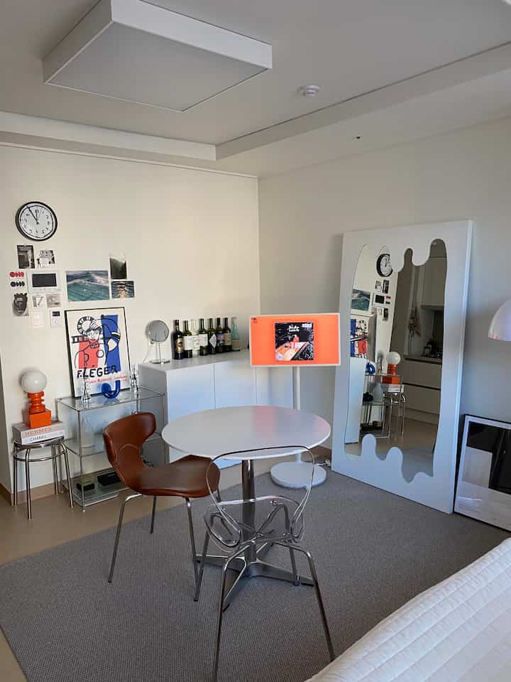 White and brown toned living room with a round table, two chairs, and a large uniquely designed mirror creating a stylish space