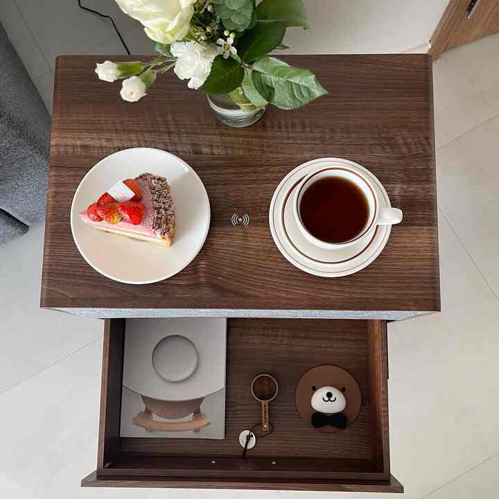 A cozy home cafe scene featuring a wood-tone side table with a coffee cup and slice of cake in white dishware