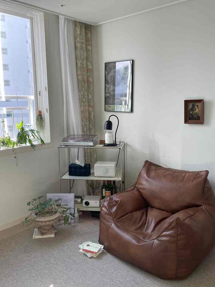 Natural tone small living room featuring brown leather bean bag, rug, turntable and candle on shelf creating cozy ambiance