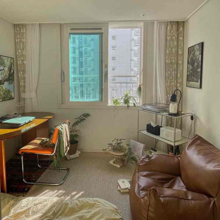 Natural-toned small single household workspace and relaxation room featuring brown leather armchair, wooden desk, and plants with cozy atmosphere