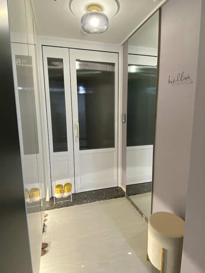 白を基調としたウッドトーンのフレンチカントリー風玄関、大きな鏡とベージュのスツールが配された落ち着いた印象のインテリア