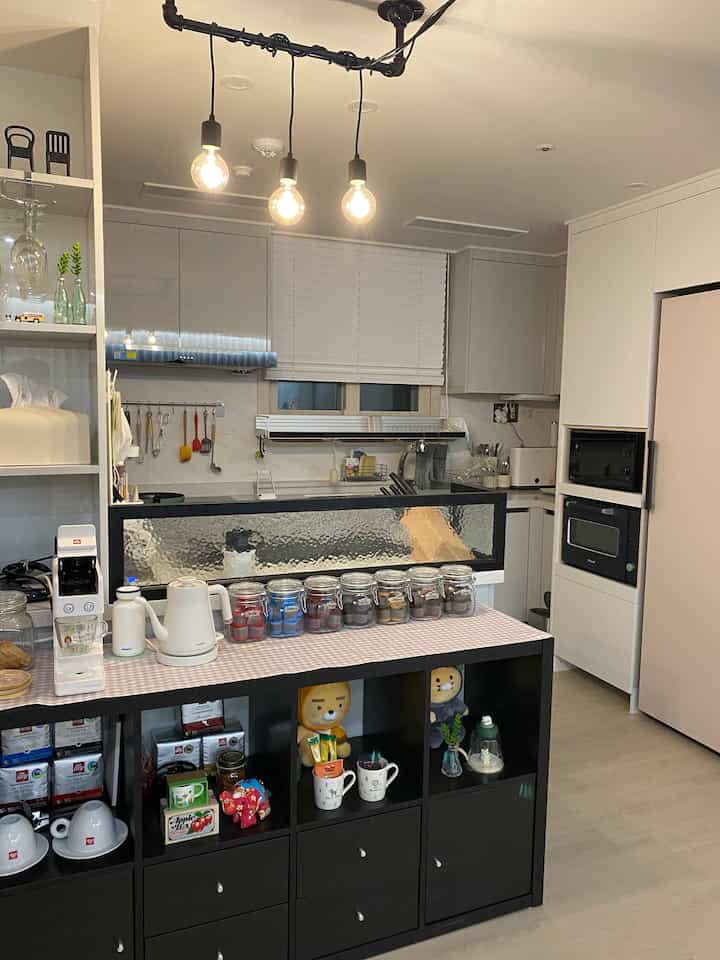 A white and black toned kitchen space featuring a black Kallax kitchen island with glass partition and pendant lights in a modern home cafe setup