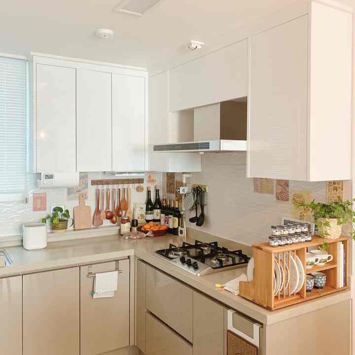 Bright white and natural wood-tone L-shaped kitchen featuring wooden utensils and plants for a cozy atmosphere