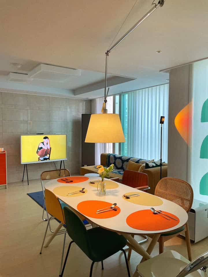 White and orange-toned living room dining area featuring a central pendant light and assorted chairs, creating a cozy interior