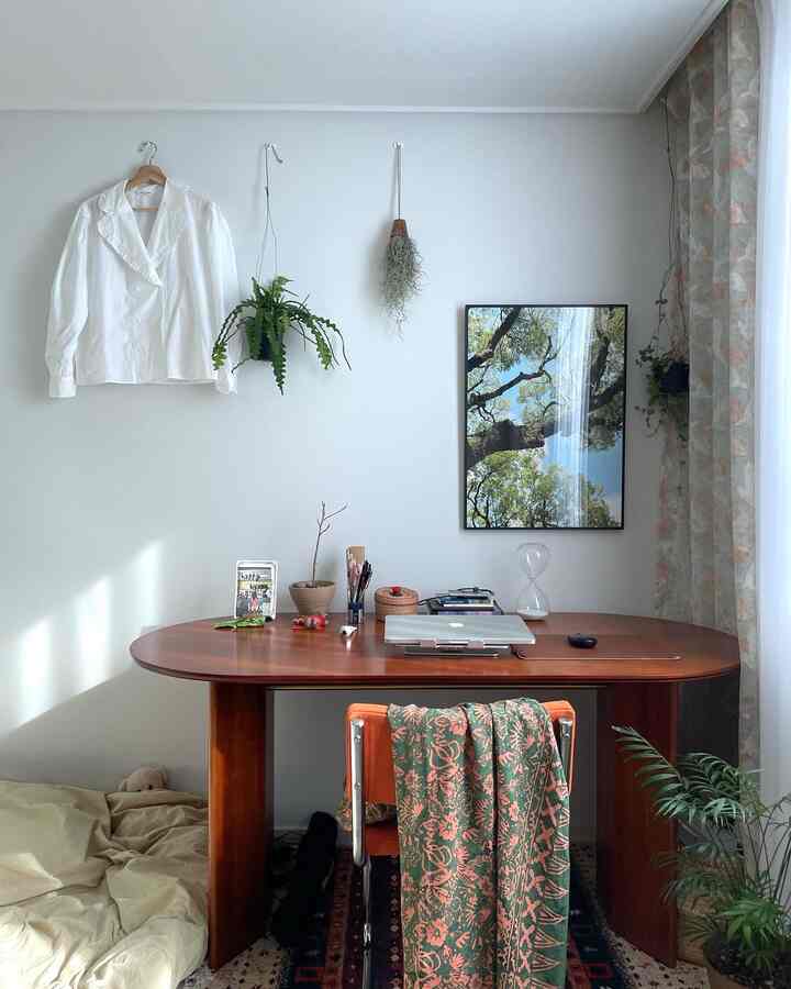 White walls and wood-tone desk in a vintage-inspired small workspace with plants and curtains