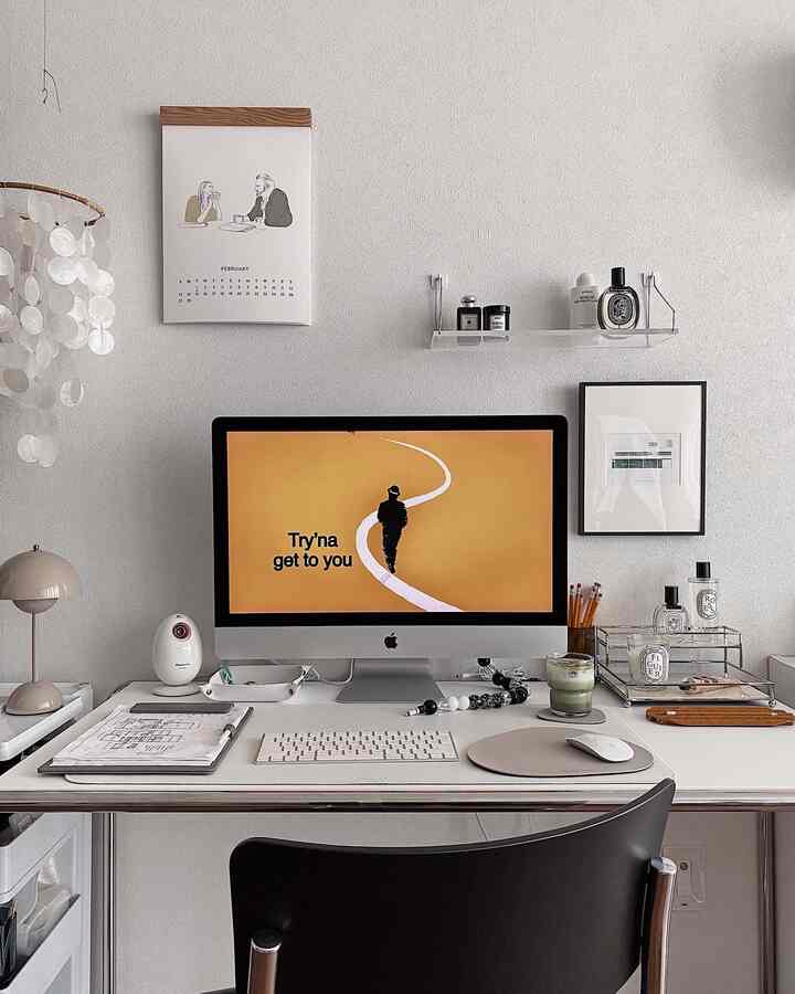 White and beige toned compact home office featuring an iMac, desk mat, mobile, and picture frame for a clean workspace