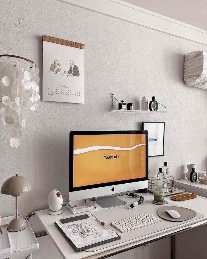 White and beige toned home office space featuring a clean desk with computer and lamp, giving a simple modern vibe