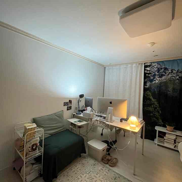 A small bedroom home office with white and green tones featuring a sofa and dual computers on a desk, creating a cozy atmosphere