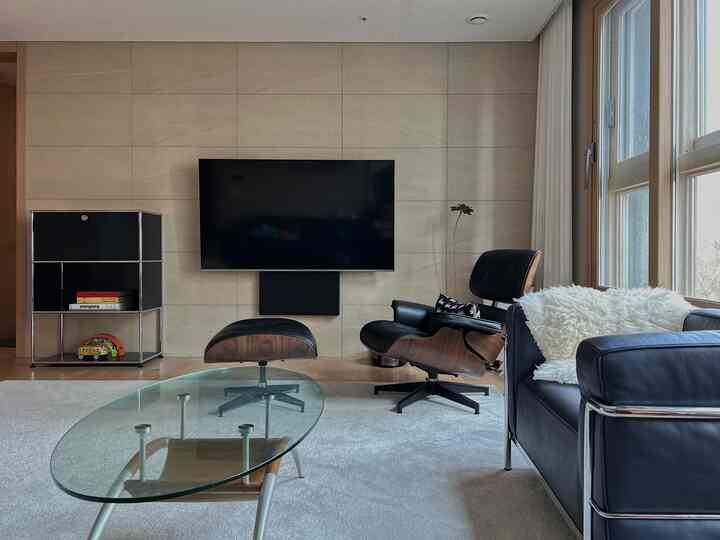 A sophisticated living room with wood tones and black elements, featuring a mid-century modern armchair and glass coffee table.