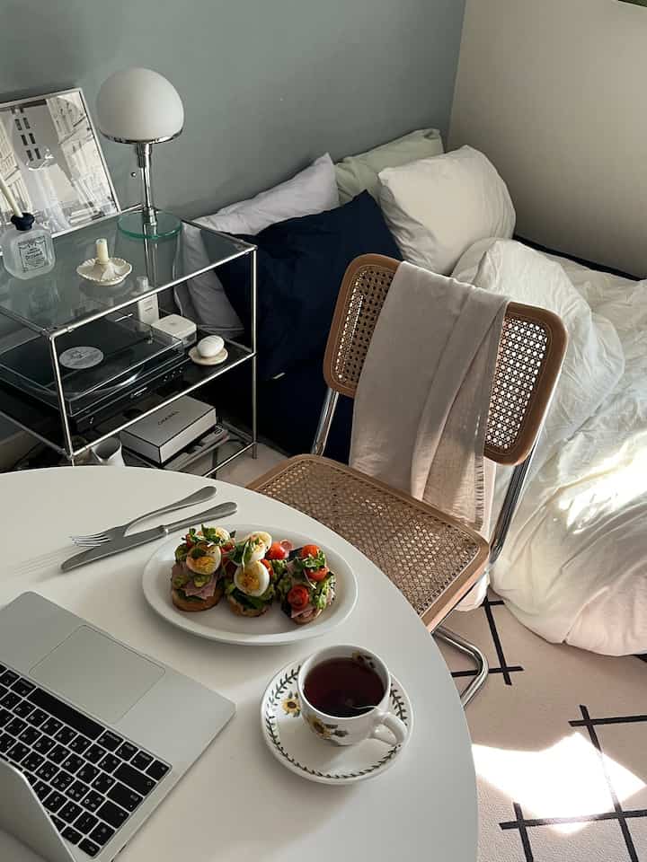 白とベージュのトーンのワンルーム寝室、丸いダイニングテーブルとラタンチェアが配置された雰囲気のあるモダンな空間