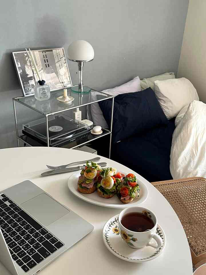 ホワイトとネイビートーンのワンルーム寝室、丸テーブルにブランチとノートパソコンが配置された印象的な空間