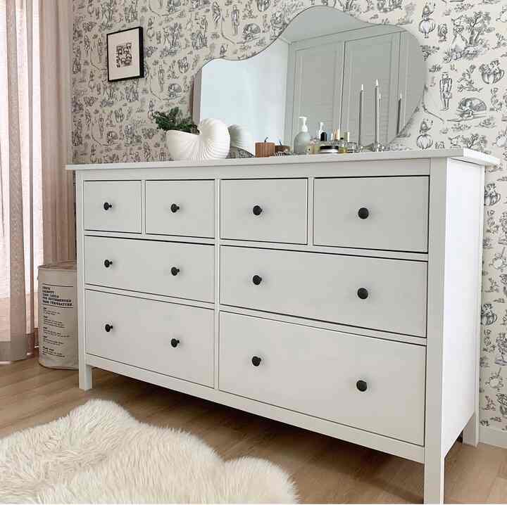 ホワイトとナチュラルウッドトーンが調和したウォークインクローゼット、大きな白いドレッサーと模様のアクセント壁紙が印象的な清潔感のある空間