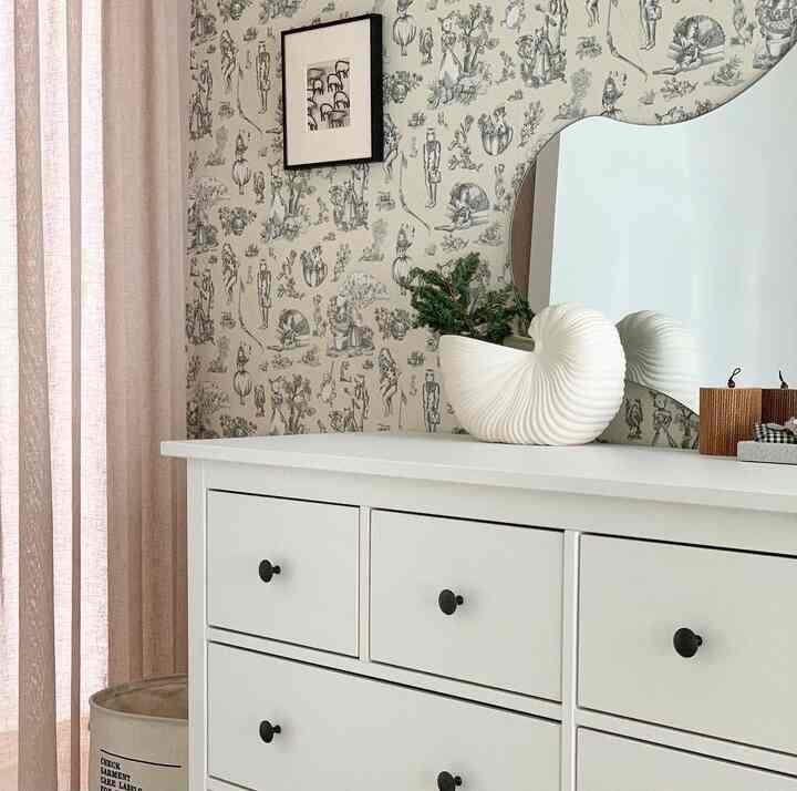 白を基調としたウォークインクローゼット、白いドレッサーと変形ミラー、アクセント壁紙が配置された雰囲気のあるインテリア