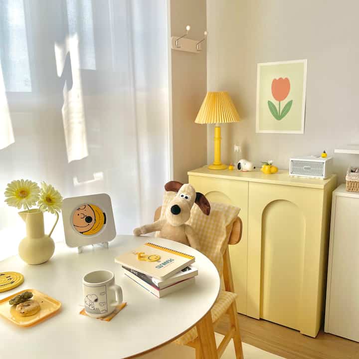 Warm yellow and natural-toned living room featuring a round table, table lamp, and a floral poster creating a cozy atmosphere