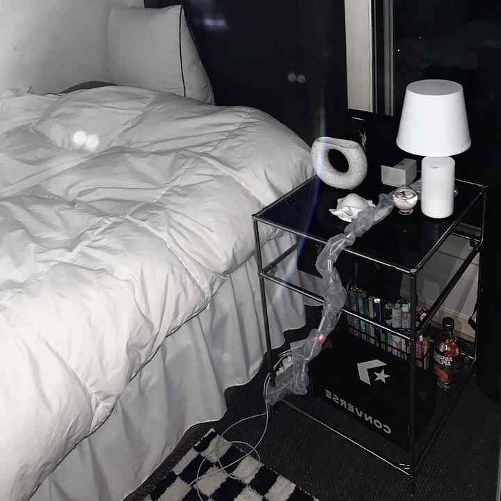 白と黒のモダンな寝室、ベッドとガラスのナイトテーブルにランプが置かれたシンプルで落ち着いた空間