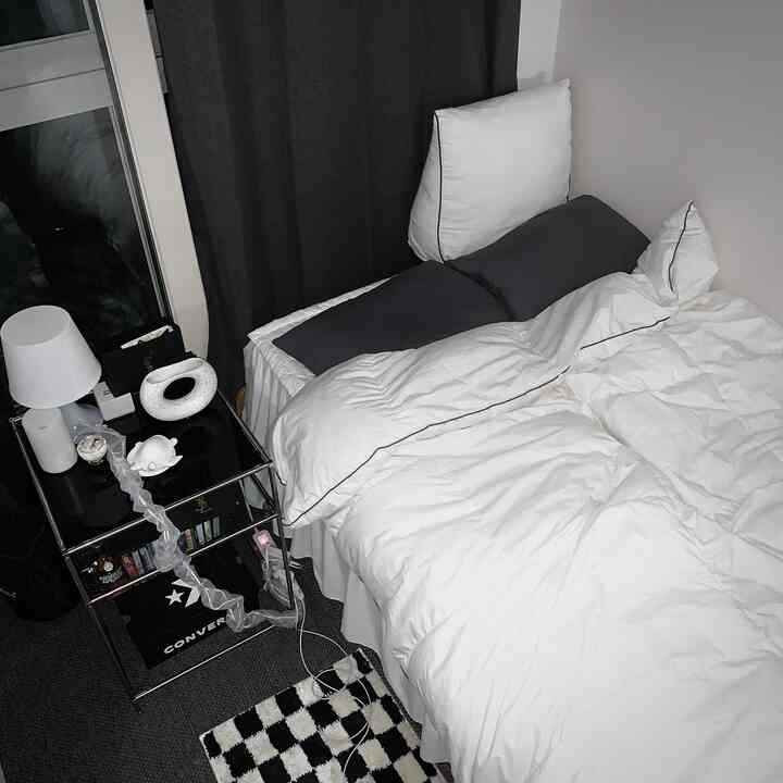 黒と白のトーンの寝室、白いベッドと黒のナイトテーブル、チェック柄のラグがあるモダンな空間