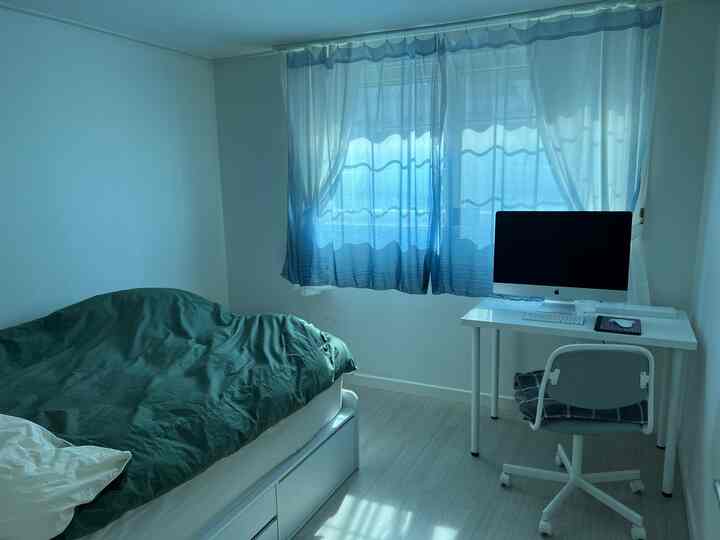 White-walled small bedroom for single household featuring green bedding on bed and white desk with computer, creating a cozy atmosphere