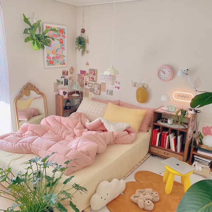 Cozy bedroom in pink and ivory tones featuring a warm duvet, multiple plants, and soft ambient lighting