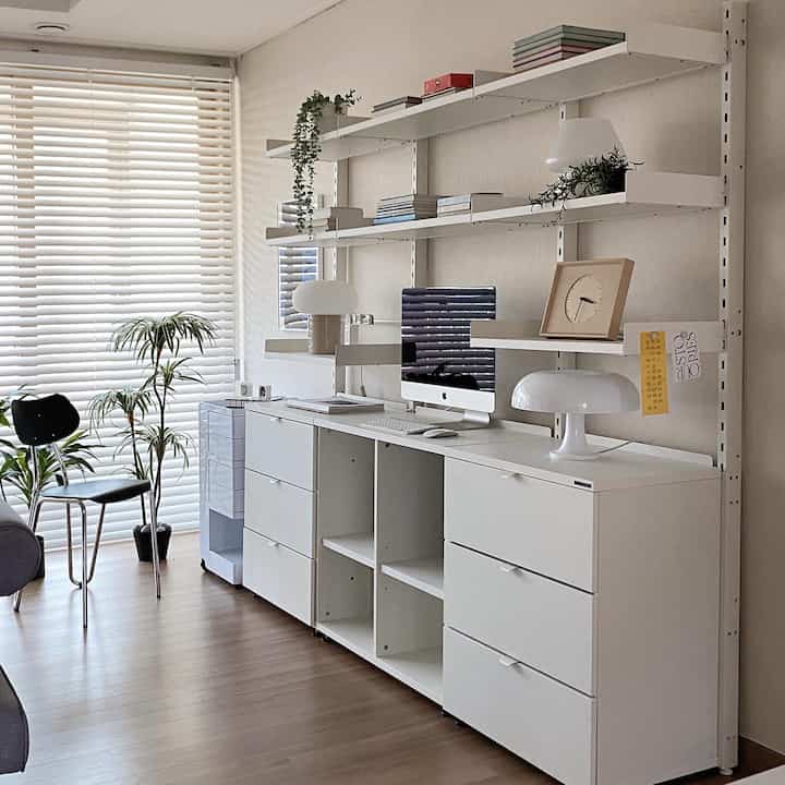 White and wood tone home office space featuring desk, bookshelf, and plants with a clean modern atmosphere