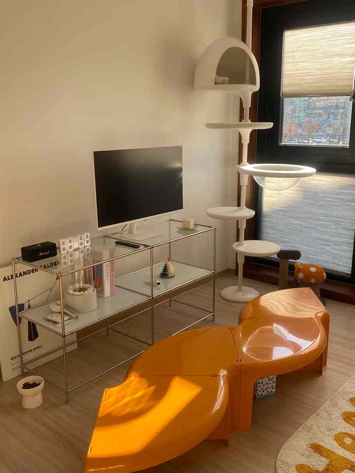 オレンジ色のモジュールソファテーブルと白いキャットタワーが配置された、ミッドセンチュリーモダンスタイルのリビング