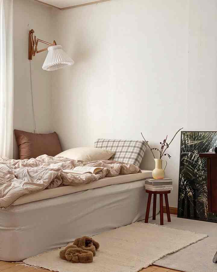 Beige and brown toned bedroom featuring plush bedding, wooden stool with vase, creating a cozy atmosphere