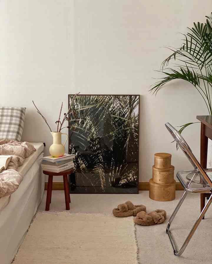 Beige and white toned living room featuring a sofa bed, wooden stool, and plant poster with a cozy natural style