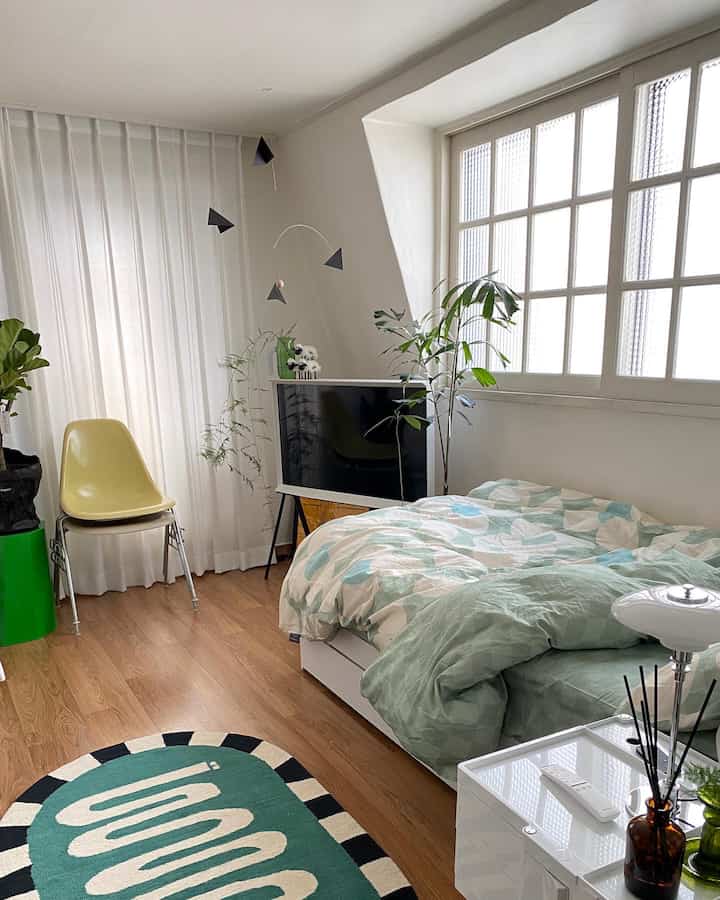 Green and white toned studio bedroom featuring bed, simple furniture, and plants with a natural atmosphere