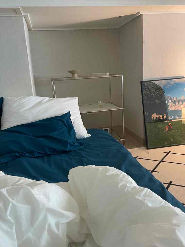 A simple and modern bedroom with white and navy tones featuring neat bedding and a metal modular shelf