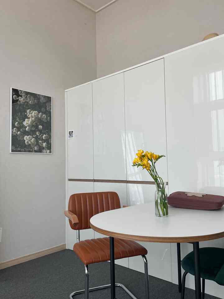 Bright white living room with storage cabinets, round dining table and brown chair creating a clean, cafe-style atmosphere