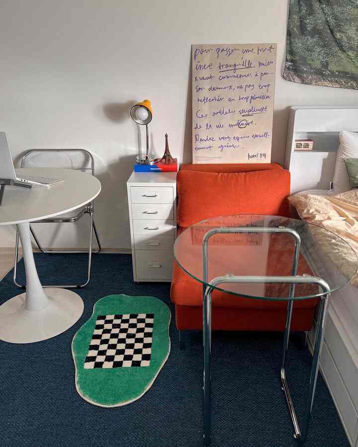 White and orange toned studio apartment featuring transparent glass table, compact desk, and sofa creating a cozy workspace