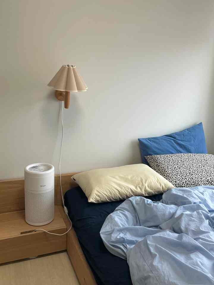 白い壁とナチュラルウッドのベッドフレームがある小さな寝室、青と黄色の枕が置かれた落ち着いた雰囲気のインテリア