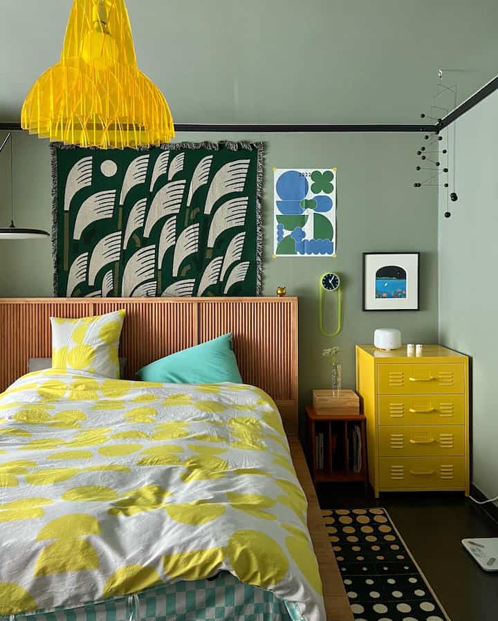 Mid-Century Modern bedroom with green-toned walls and yellow chest of drawers, featuring a cozy atmosphere with polka-dot yellow bedding