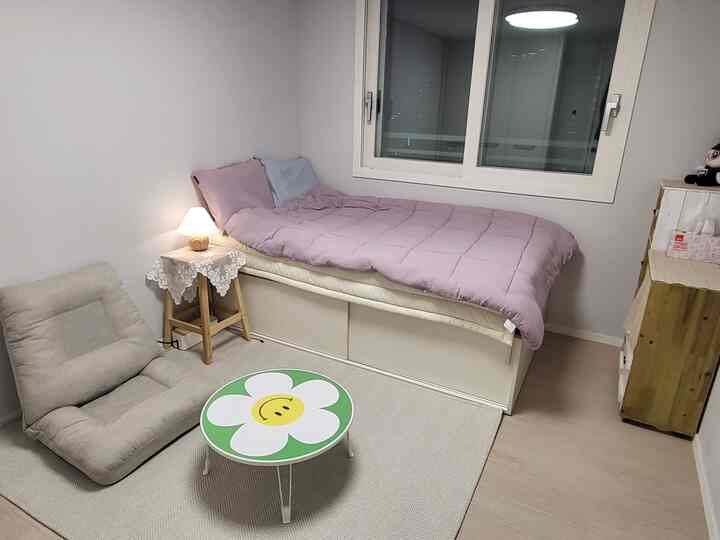 ナチュラルカラーの寝室、ベッドとナイトテーブル、低い椅子と小さな丸テーブルが配置された雰囲気のあるインテリア