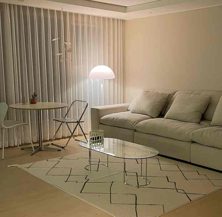Beige and white toned living room featuring large sofa, transparent coffee table, and floor lamp creating a cozy modern space