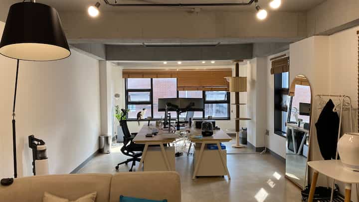Modern home office with white walls and wood-toned blinds, featuring a cat and cat tower by the window in a tidy workspace