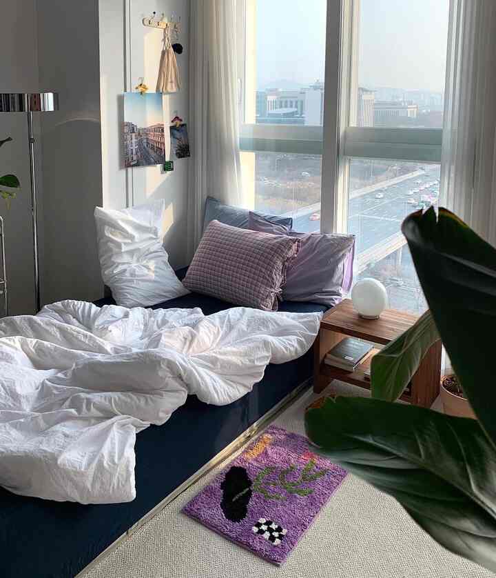 Studio bedroom with white and navy bedding featuring purple accent rug and curtains in a modern setting